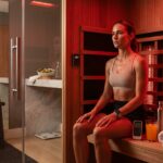 Athlete in a glowing infrared sauna sweating, with thermometer, water bottle, smartwatch and recovery gear visible to illustrate sauna protocols for recovery, metabolism and longevity